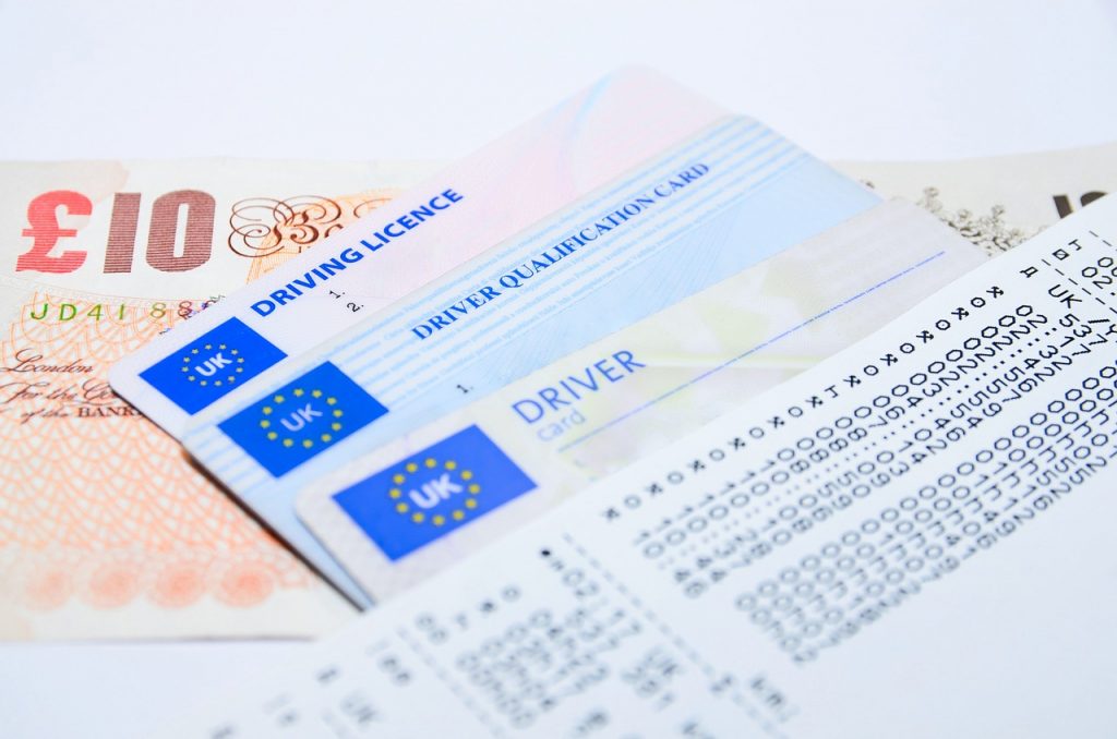 a photo of three different UK driving licenses on top of a £10 note and under a receipt.